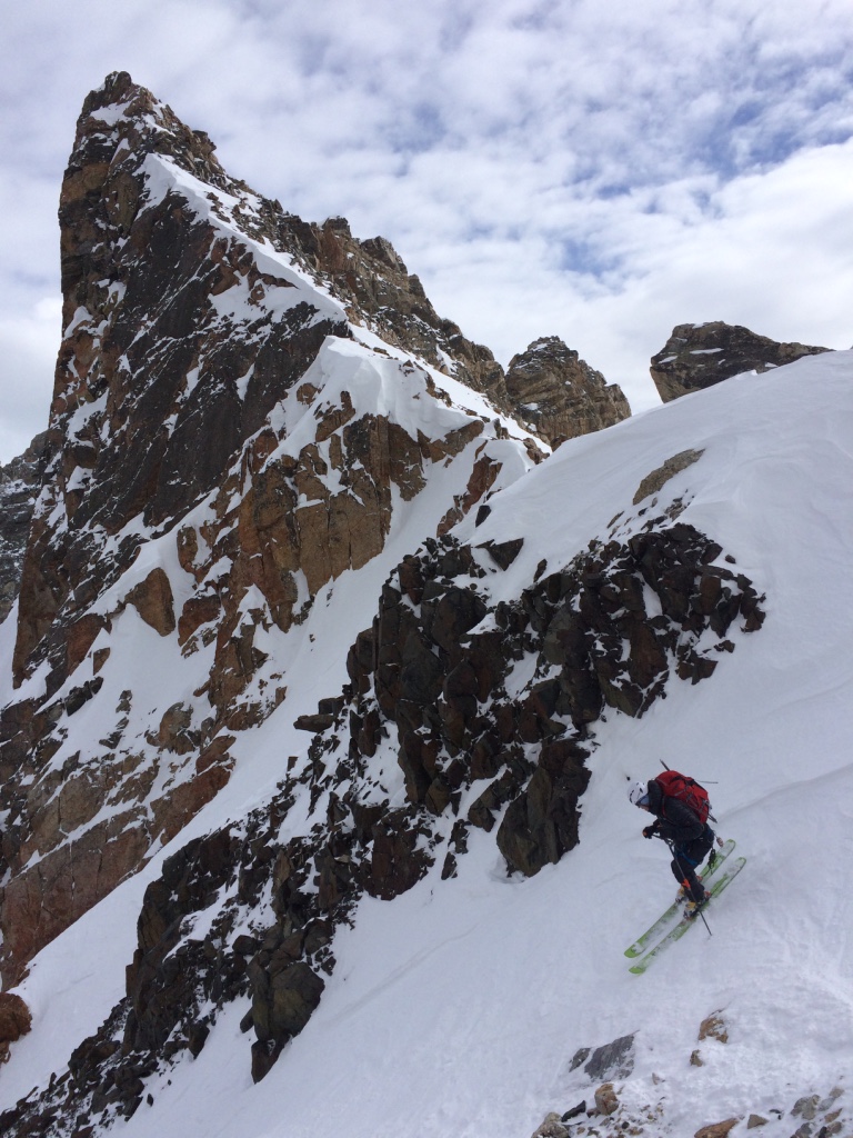 A ski mountaineer is starting a descent down a high-altitude ski run beneath a typical peak in the Grand Tetons National Park.