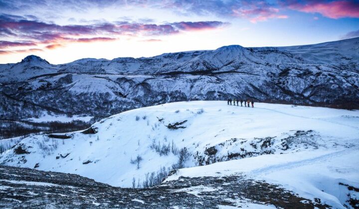 A group of hikers seen from the distance. Beautiful blue and pink sky in the background.