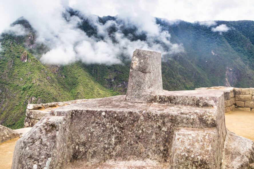 A close-up look at the ceremonial stone located in Machu Picchu with the ever-present clouds in the background.
