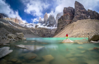 Hiker in red jacket admiring 3 peaks at Base de las Torres viewpoint in Torres del Paine, Patagonia