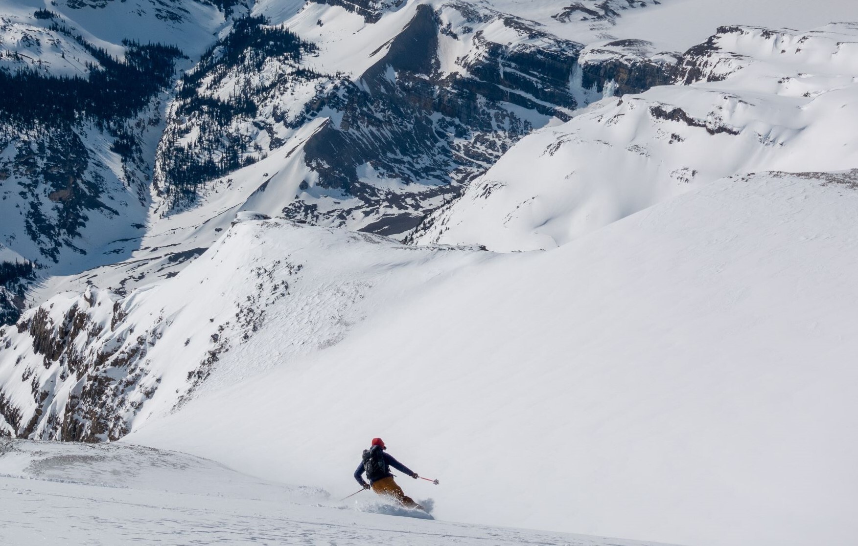 A backcountry skier going down the slope with plenty of champagne powder overlooking the mountains and valleys around Revelstoke and Golden.