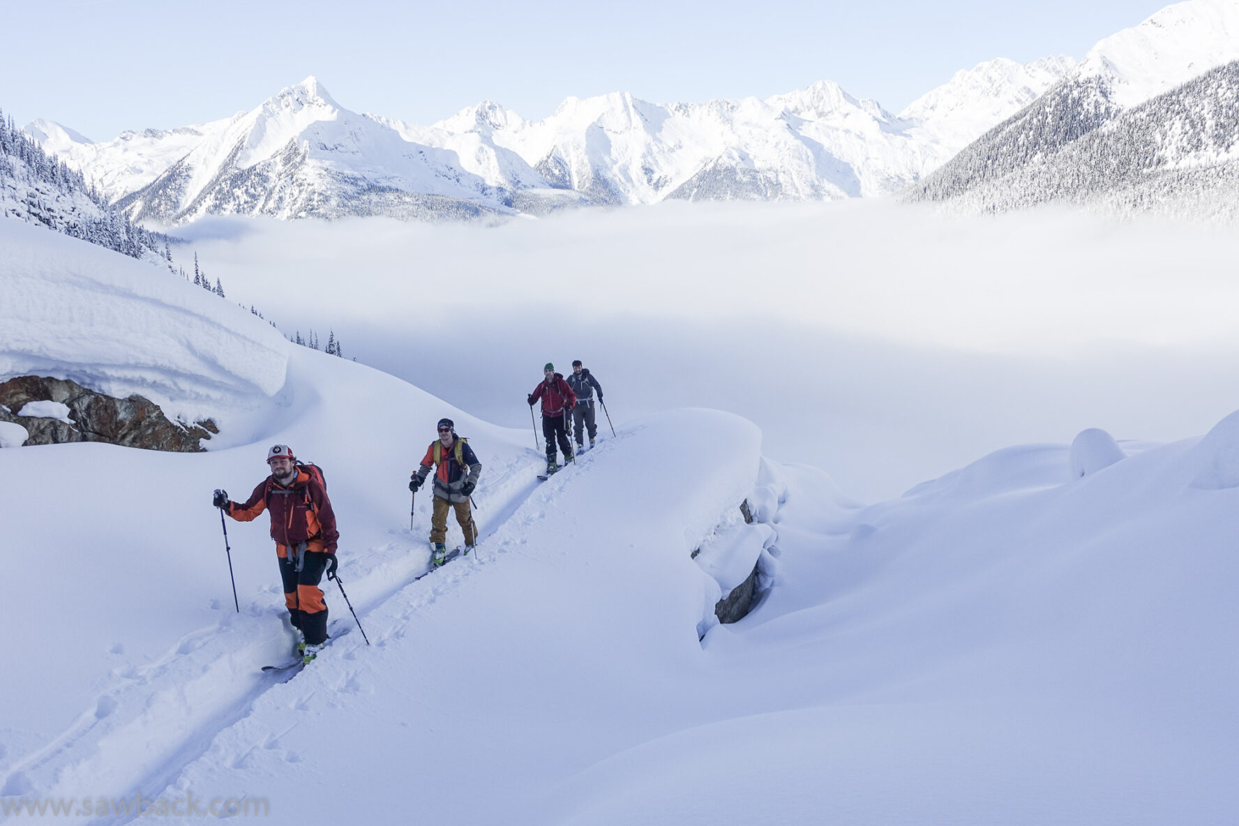 Three backcountry skiers moving in the mountains around Revelstoke and Golden with snow-dusted peaks in the distance soaring above the clouds.
