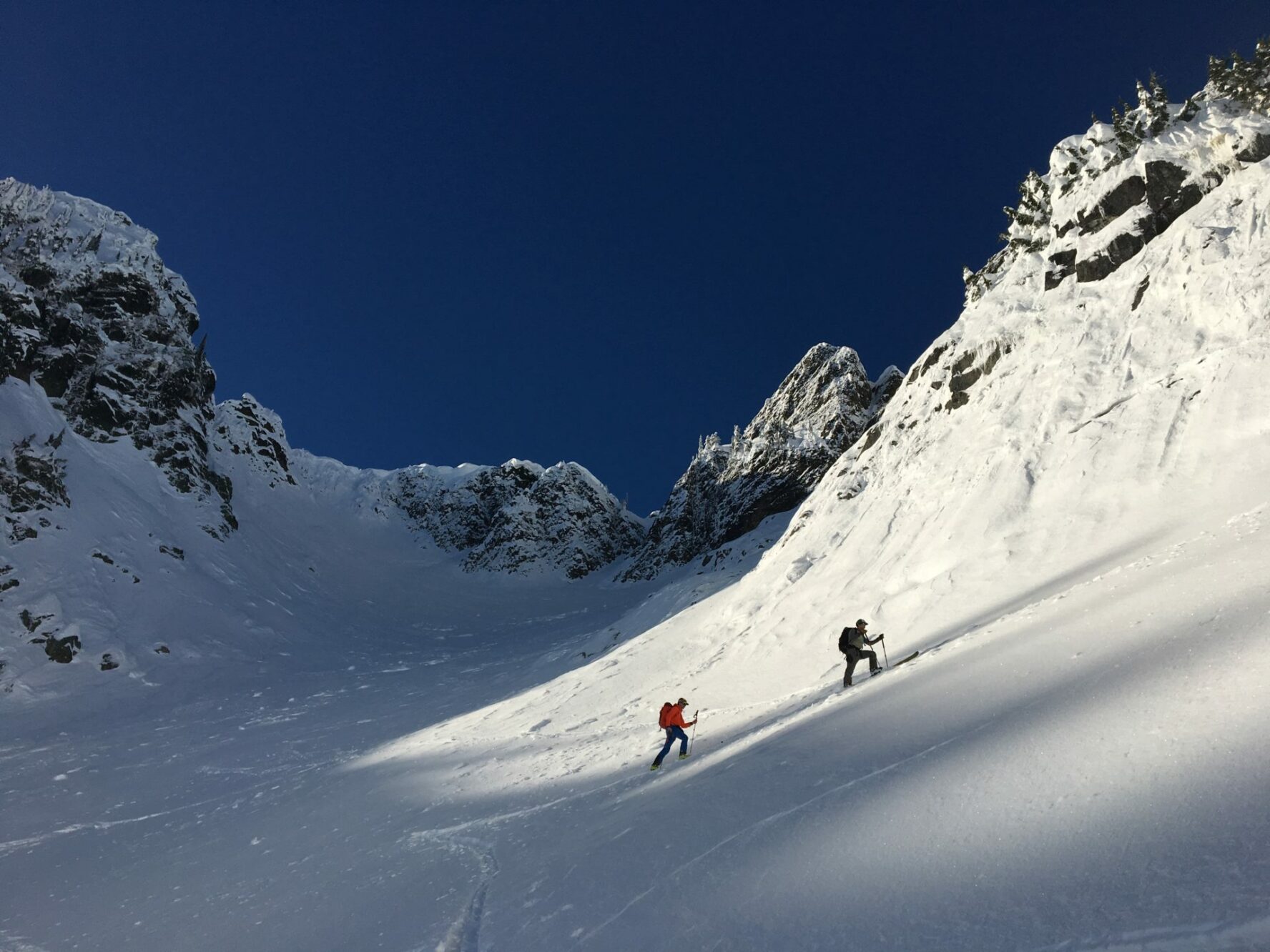 Two backcountry skiers skinning up a slope in Snoqualmie surrounded by rugged peaks.