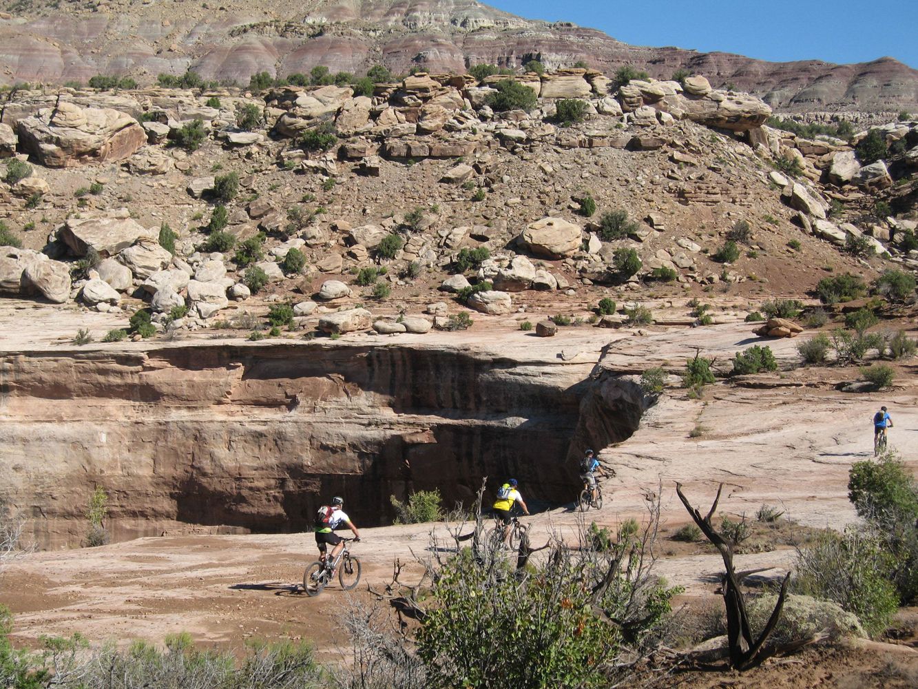 Mountain bikers navigating uneven rocky desert terrain along the Kokopelli Trail.