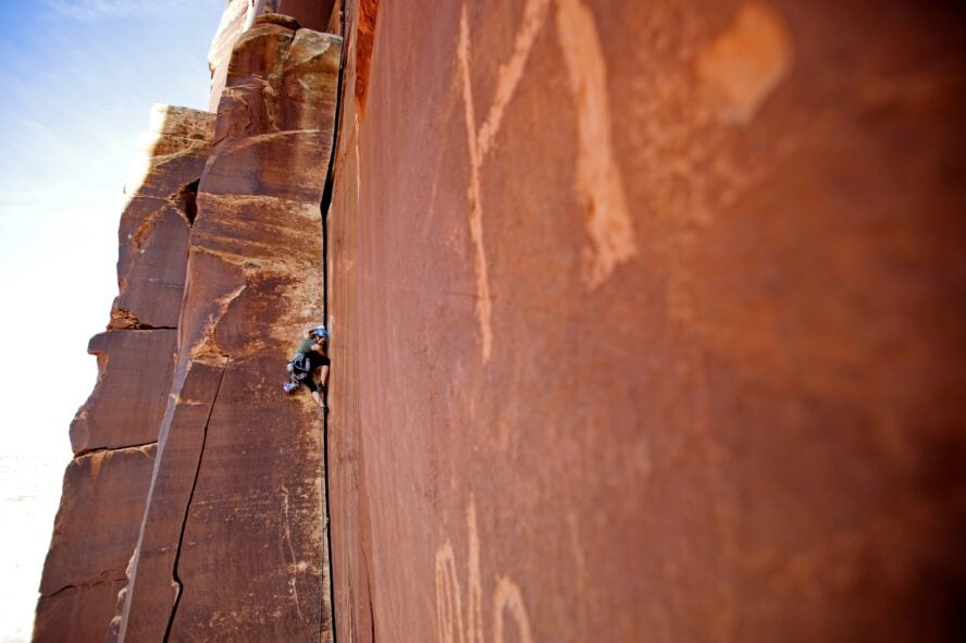  A climber on Amaretto Corner in Indian Creek, a Wingate sandstone splitter that starts as perfect hands and gets progressively wider. The route shows wear from usage and is not far from historic petroglyphs.