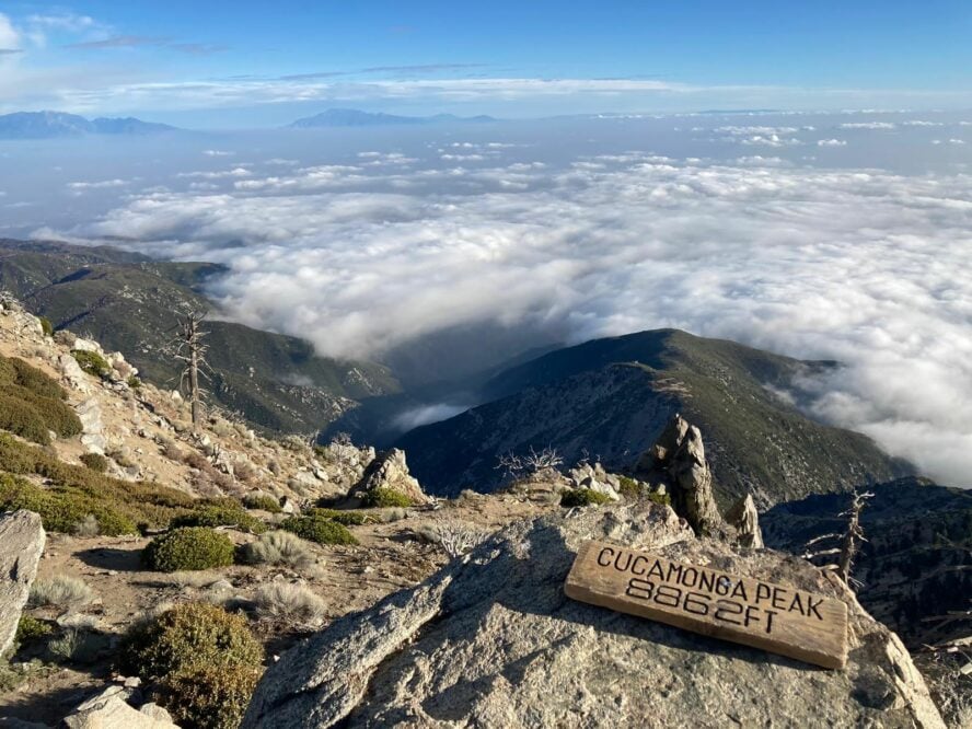 The Cucamonga Peak sign with green mountain ridges below