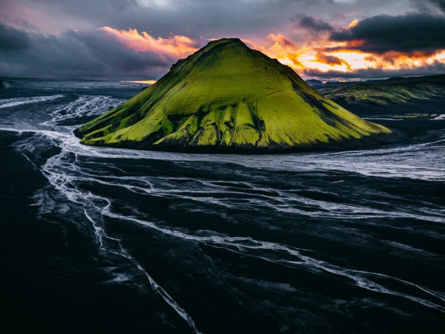 The vivid green cone of the Maelifell volcano rising from a flooded jet-black plain