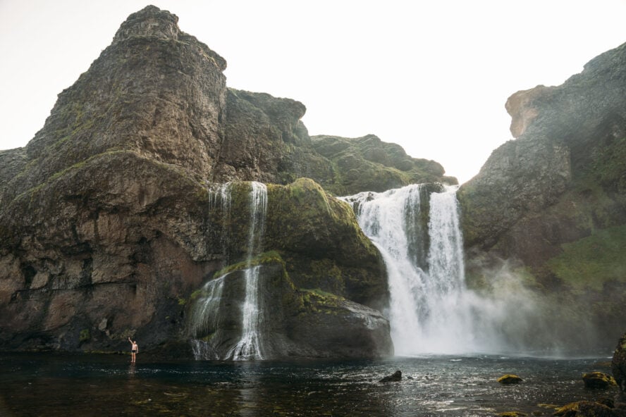 Me standing in ankle-deep shallows under a roaring waterfall in Iceland