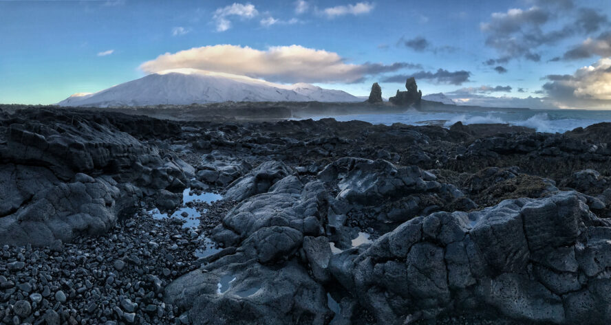 A rugged lava rock beach towered by the white, sun-kissed Snæfellsjökull volcano