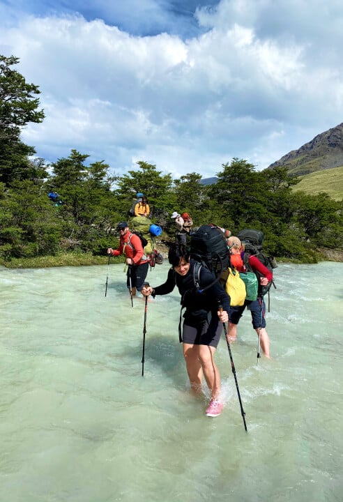 A group of trekkers crossing a river on the Huemul trek.