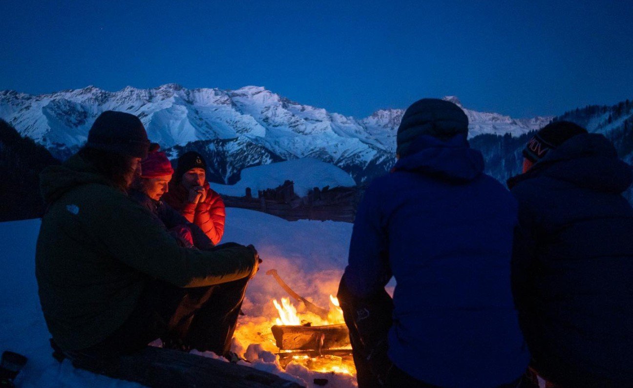 A group of backcountry skiers encircling a campfire beside their basecamp during their backcountry skiing trip in Georgia.