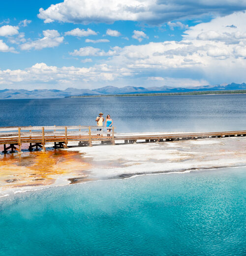 Couple relaxing and enjoying beautiful view of hot spring on vacation hiking trip. Beautiful Yellowstone Lake in the background and hot spring in foreground. Yellowstone National Park. Wyoming, USA