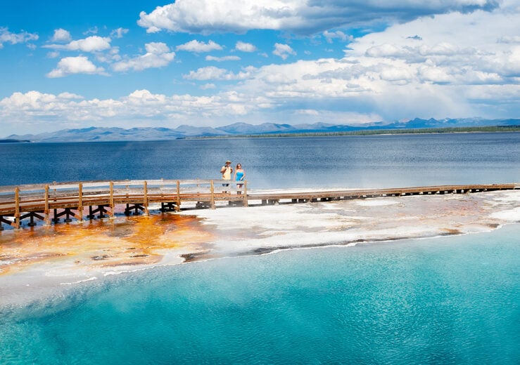 Couple relaxing and enjoying beautiful view of hot spring on vacation hiking trip. Beautiful Yellowstone Lake in the background and hot spring in foreground. Yellowstone National Park. Wyoming, USA