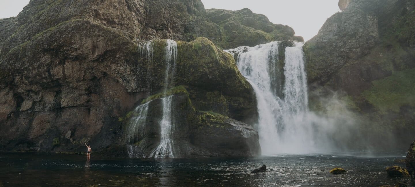 A man is just a small figure beside this waterfall in Iceland.