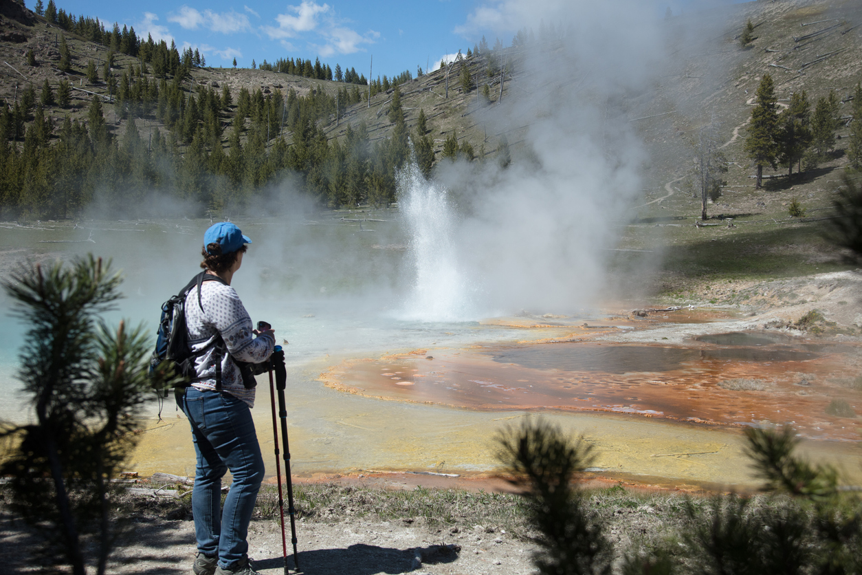 A hiker looking at an erupting geyser in Yellowstone NP