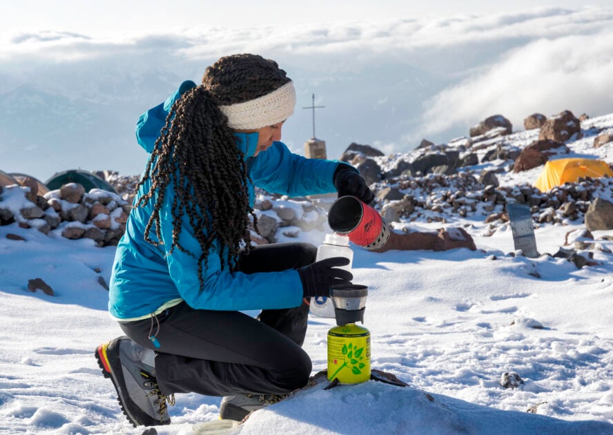 A mountaineer pours the leftover warm water from cooking with her camp stove into her water bottle.