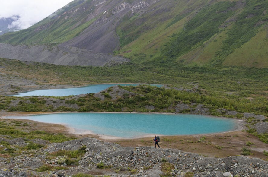 A backpacker next to a lavish blue lake 