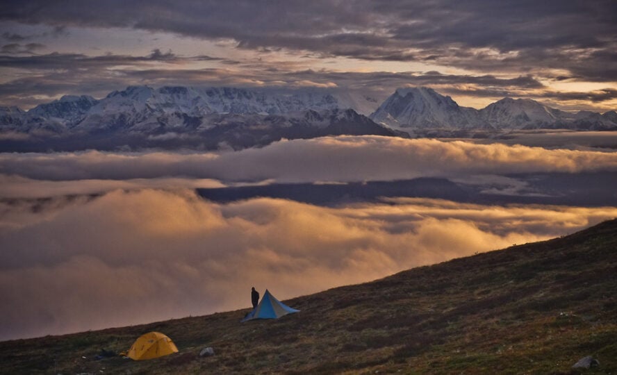  A backpacker admiring a sunset with white capped mountains and fog in the background