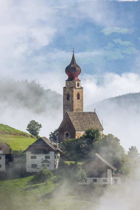 Small photogenic stone catholic church in Italian village with dramatic fog.