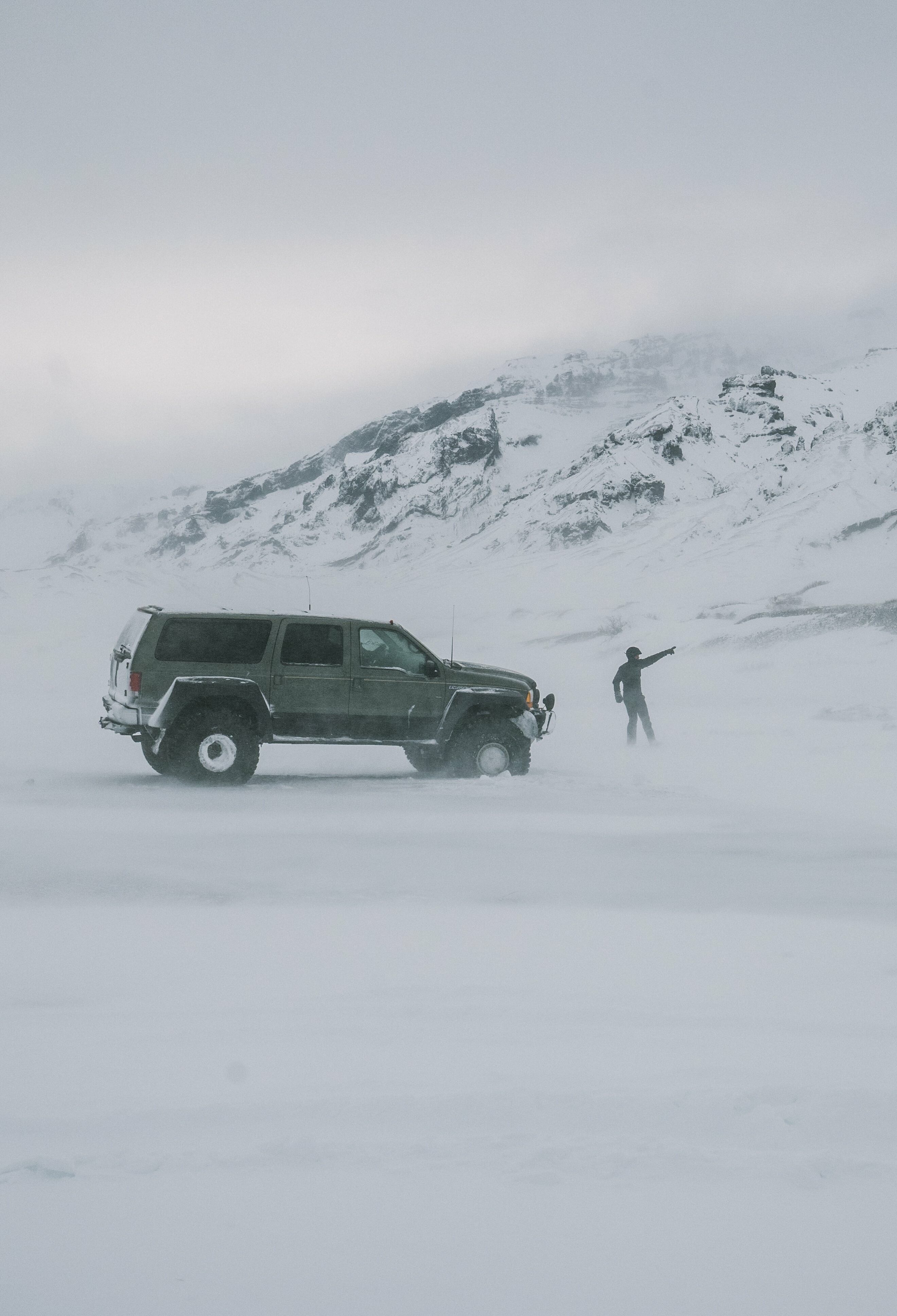 A jeep in the middle of snowy meadow and a person outside the jeep pointing at something