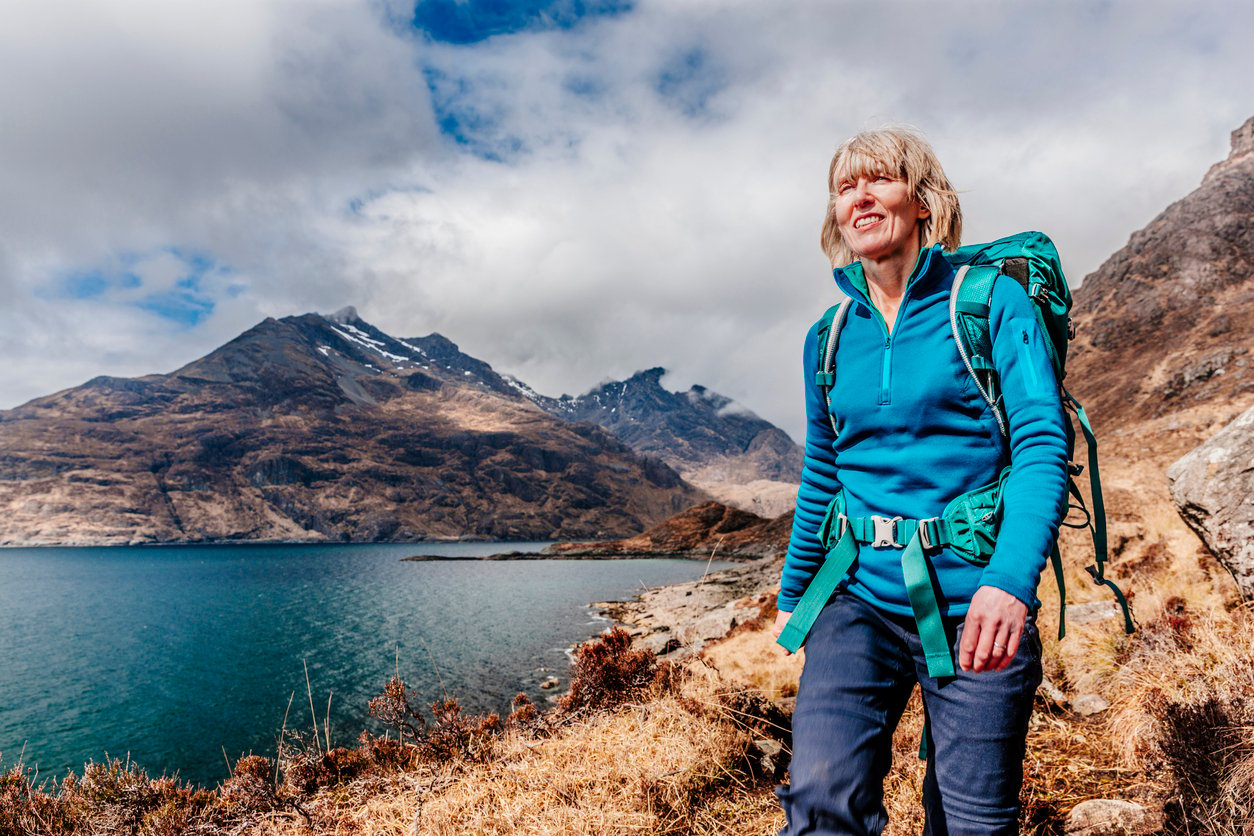 A smiling hiker walking along the shore of Loch Coruisk, the Cuillin Hills in the background