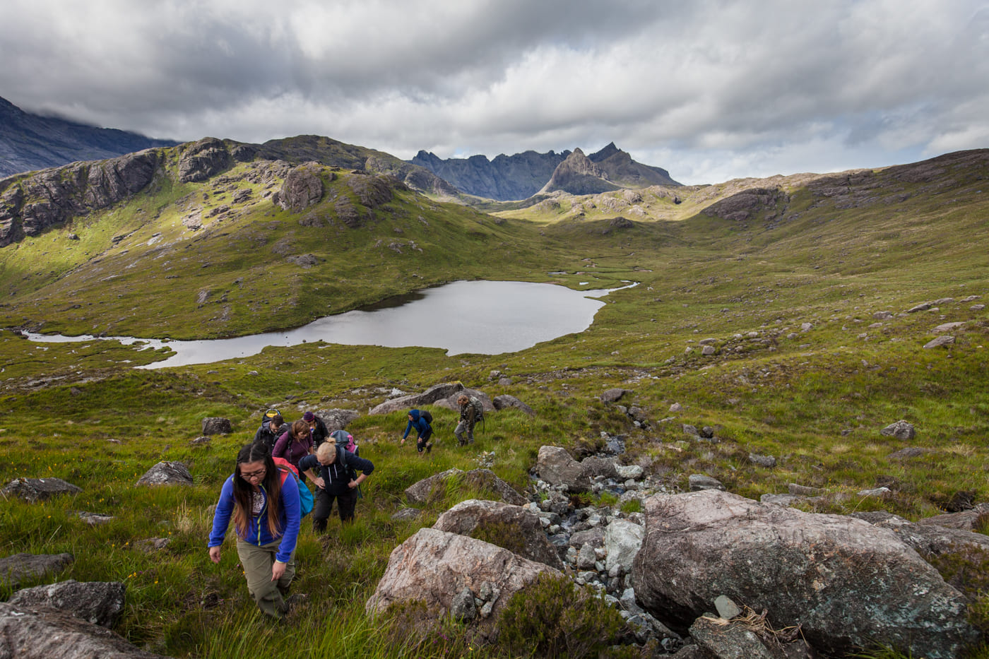 A group of hikers hiking up the mountain, loch and the Cuillin Hills in the background