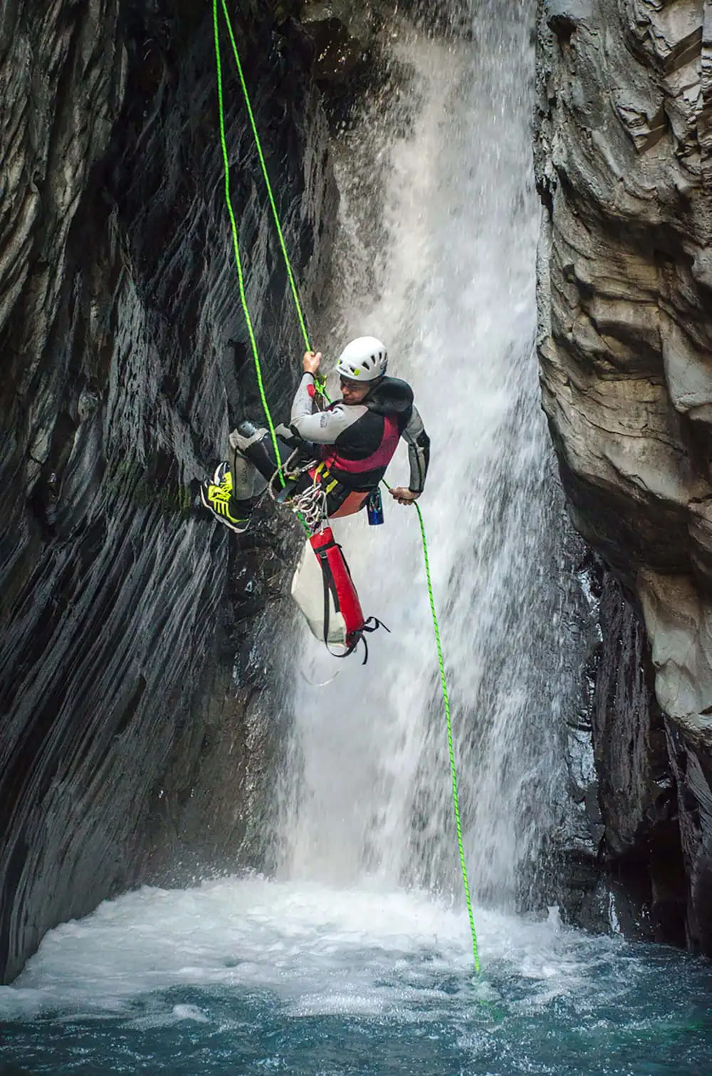 An intermediate canyoneer rappelling next to a waterfall in Bear Creek, Ouray