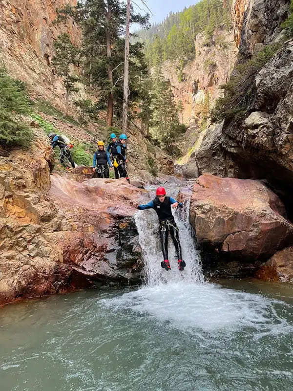 A person sliding down a small rapid in Upper Uncompahgre as other canyoneers await their turn.