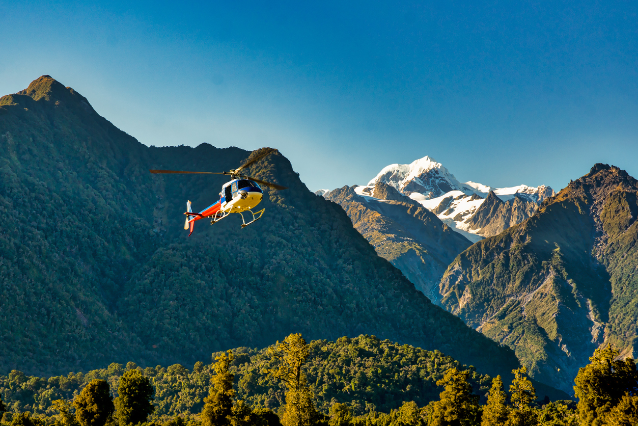 A helicopter flying over a rainforest in New Zealand’s Southern Alps