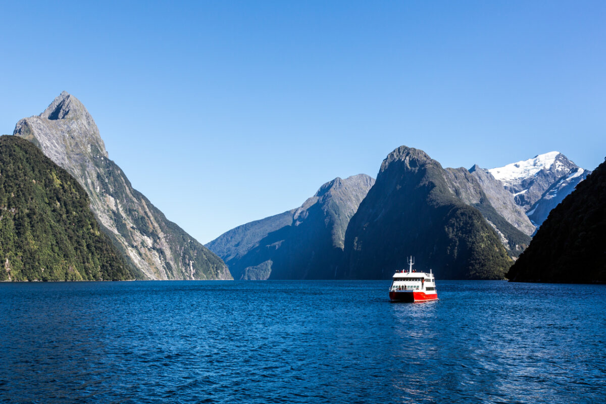View of a deep-blue lake with a boat in the middle of it and very steep mountain peaks in the background. 