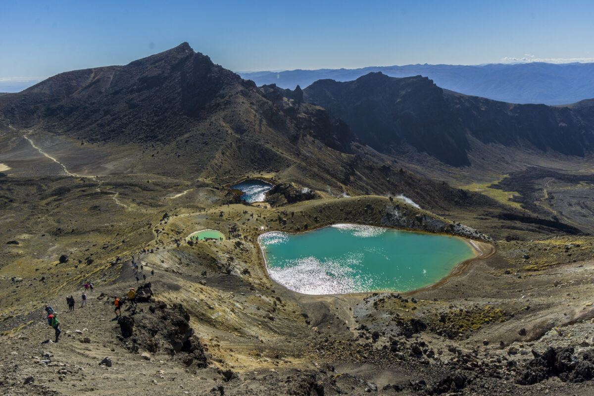 Aerial view of the turquoise lake nestled between rolling hills with a mountain peak in the distance. 