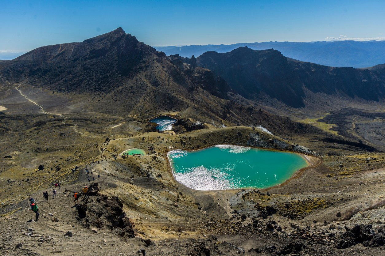Aerial view of the turquoise lake nestled between rolling hills with a mountain peak in the distance.