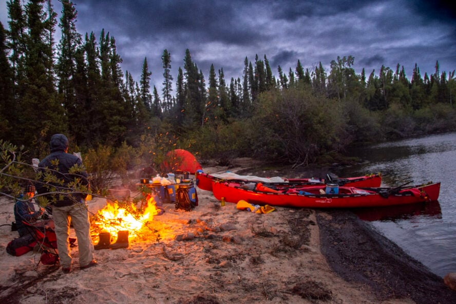 A group of canoers sitting around a fire and preparing dinner at their campsite next to Seal River in Canada