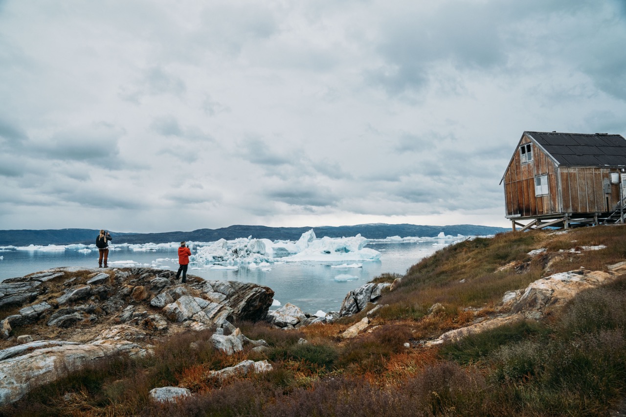 Two hikers taking photos of the icebergs from the coast