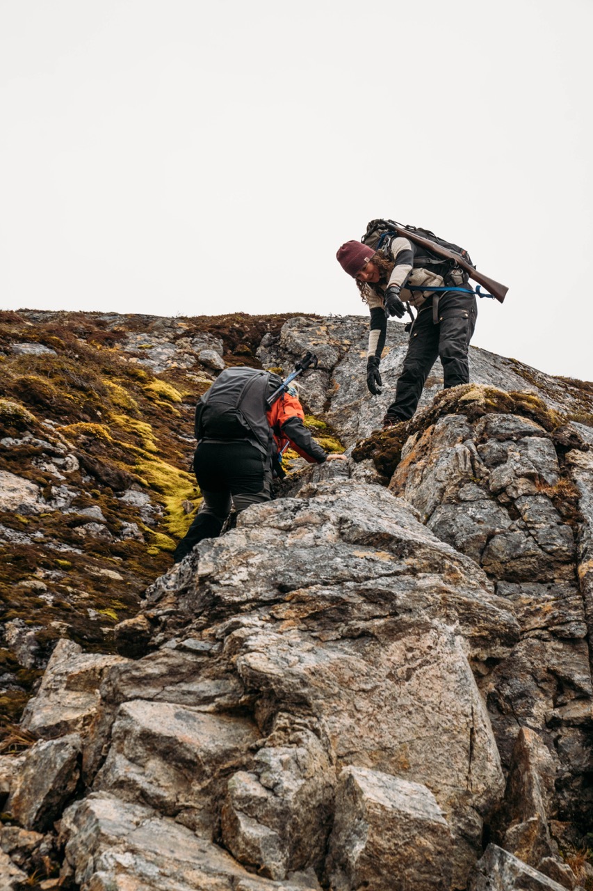 A hiker offers a hand to another hiker while climbing a slope
