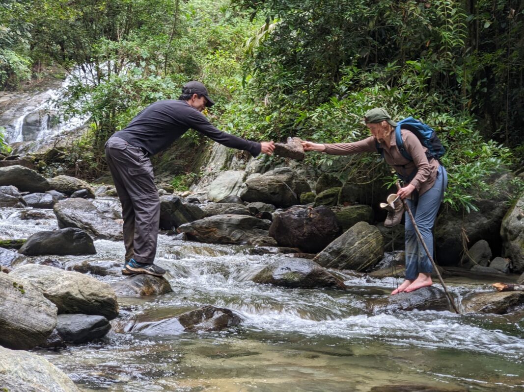 Hiker helping another hiker cross the river.