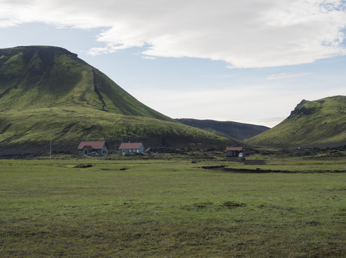 Hvanngil campsite path in lava field and green valley, small houses of hvanngil hut. volcanic mountains volcanic landscape with blue sky, Laugavegur Trail between Emstrur-Botnar and Alftavatn, central Iceland.