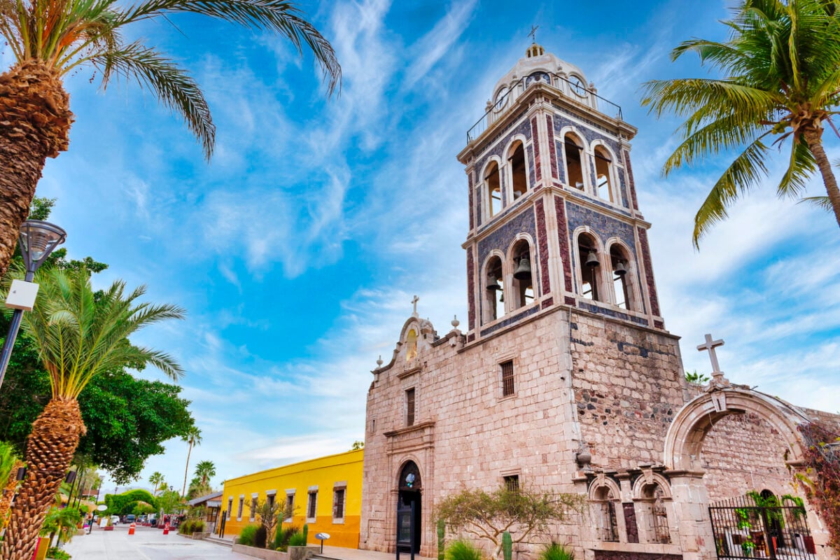 View of a church in Loreto, Mexico from the street lined with palm trees. 