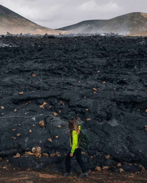 A woman hiking beside the firmed up lava close to the site of an erupting Iceland volcano.