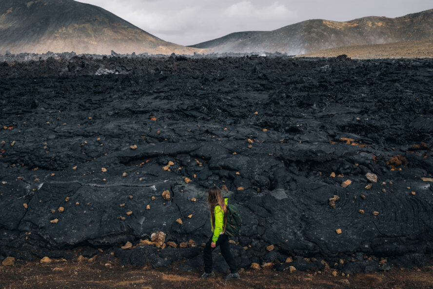 A woman hiking beside the firmed up lava close to the site of an erupting Iceland volcano.