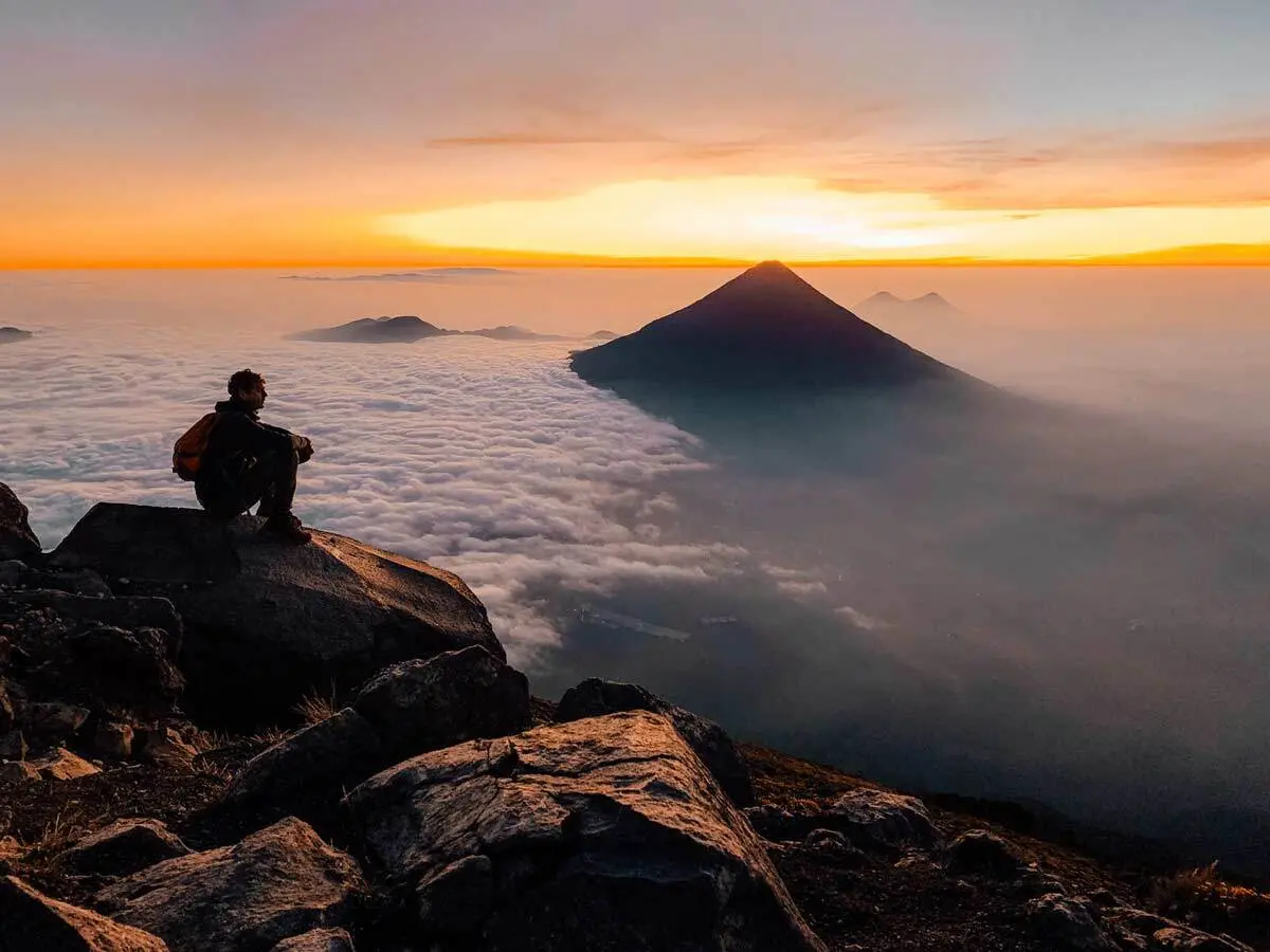 A hiker overlooking a cloudy valley on the summit of Acatenango Volcano.
