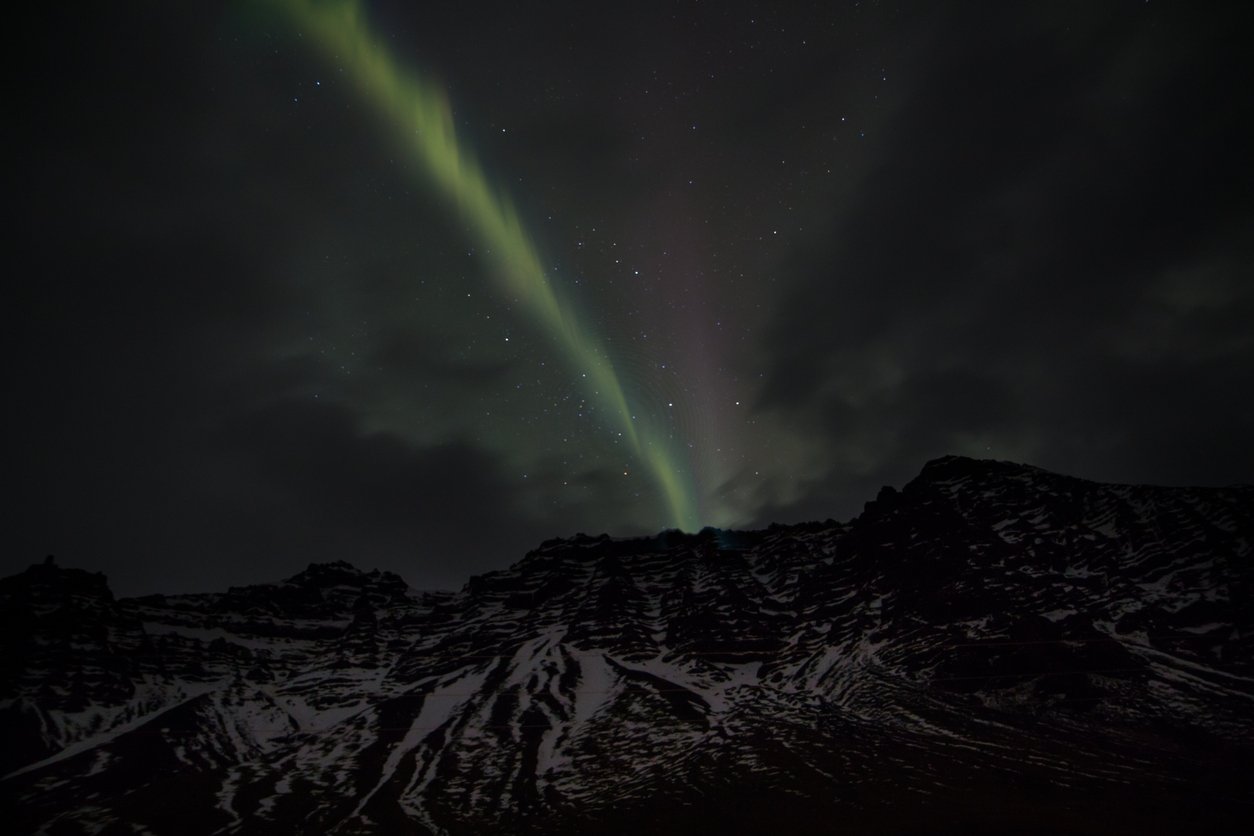 The Aurora Borealis pierces the clouds and dances behind an Icelandic glacier