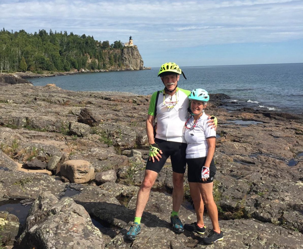 Two cyclers standing on a lake’s shore.