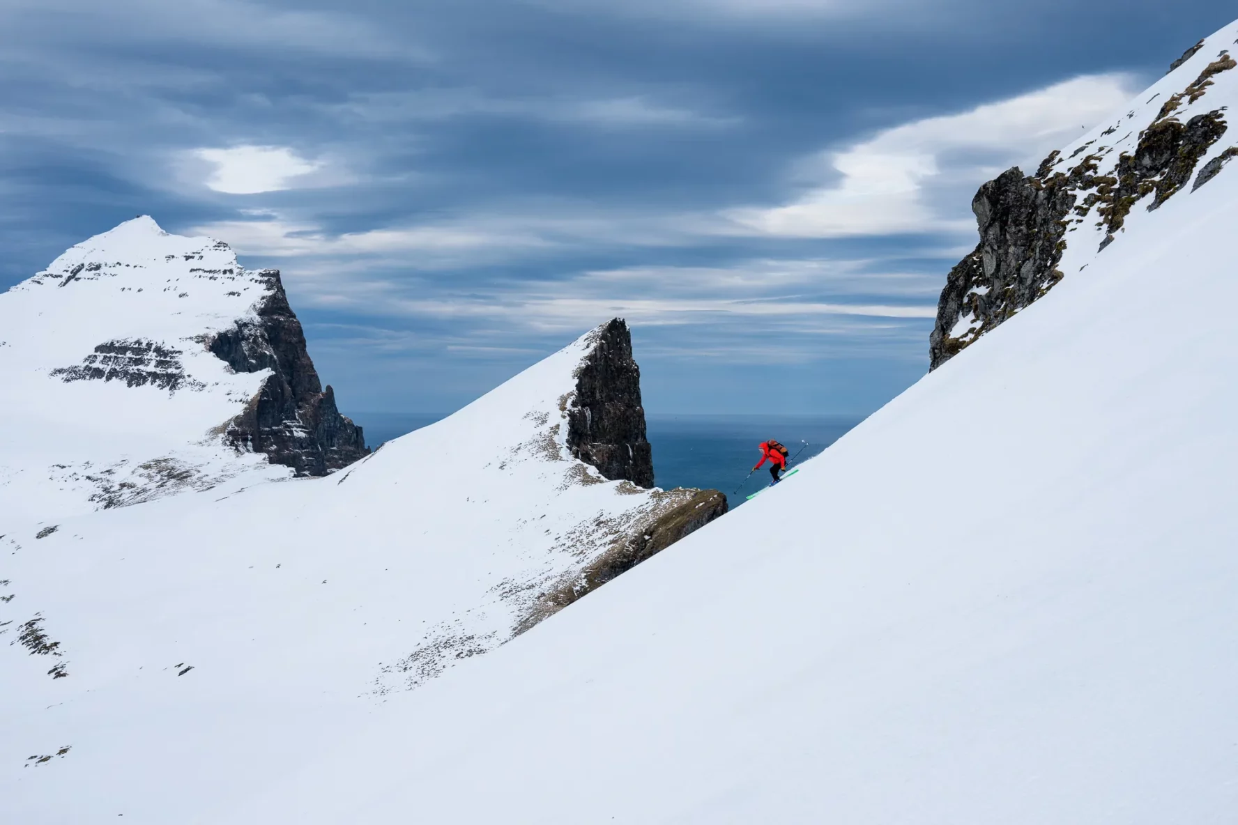 A skier skiing near a ridge with some peaks in the background in Iceland’s Westfjords.