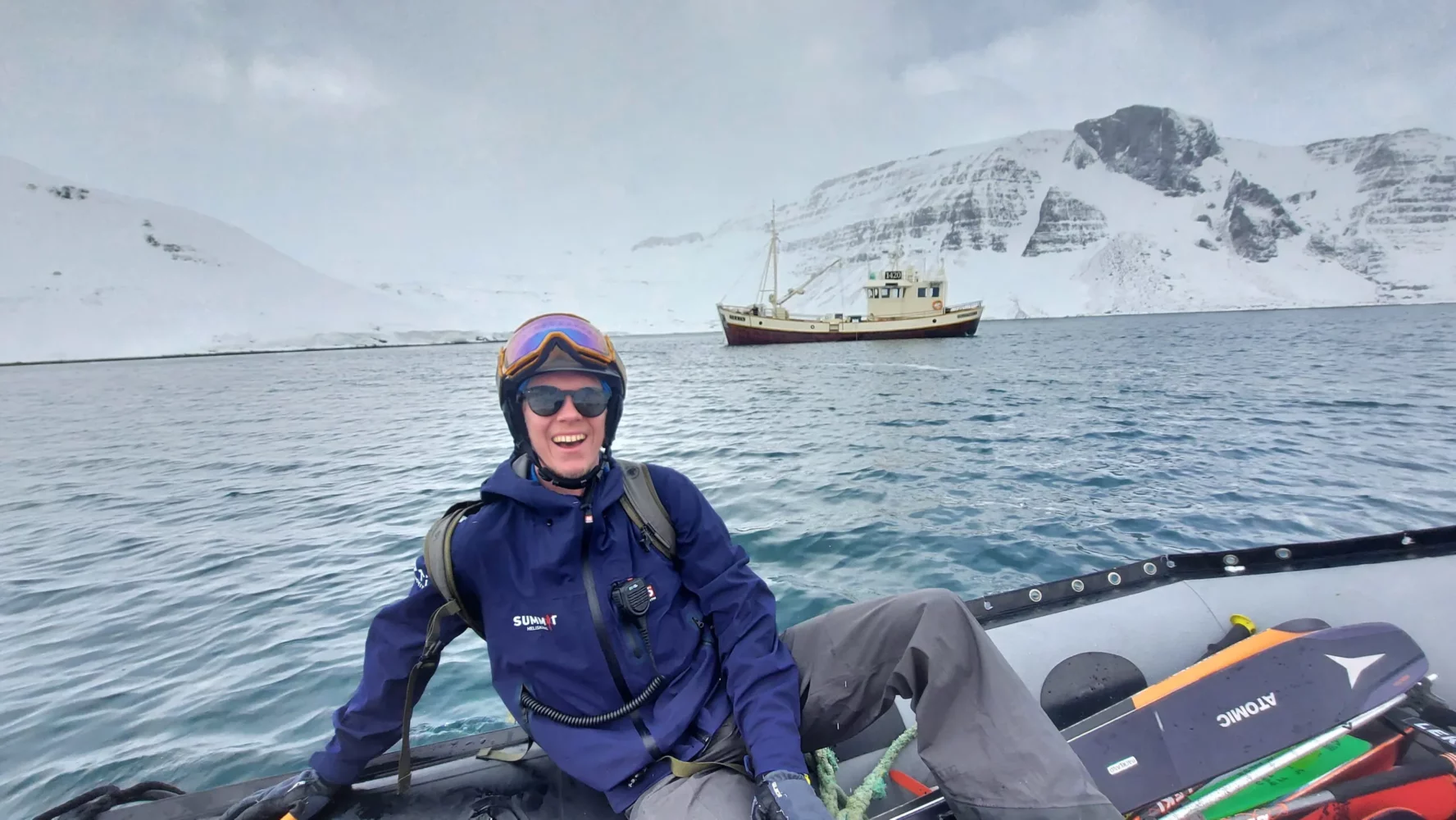 A skier smiling with a sailboat and the Icelandic seas in the backdrop.
