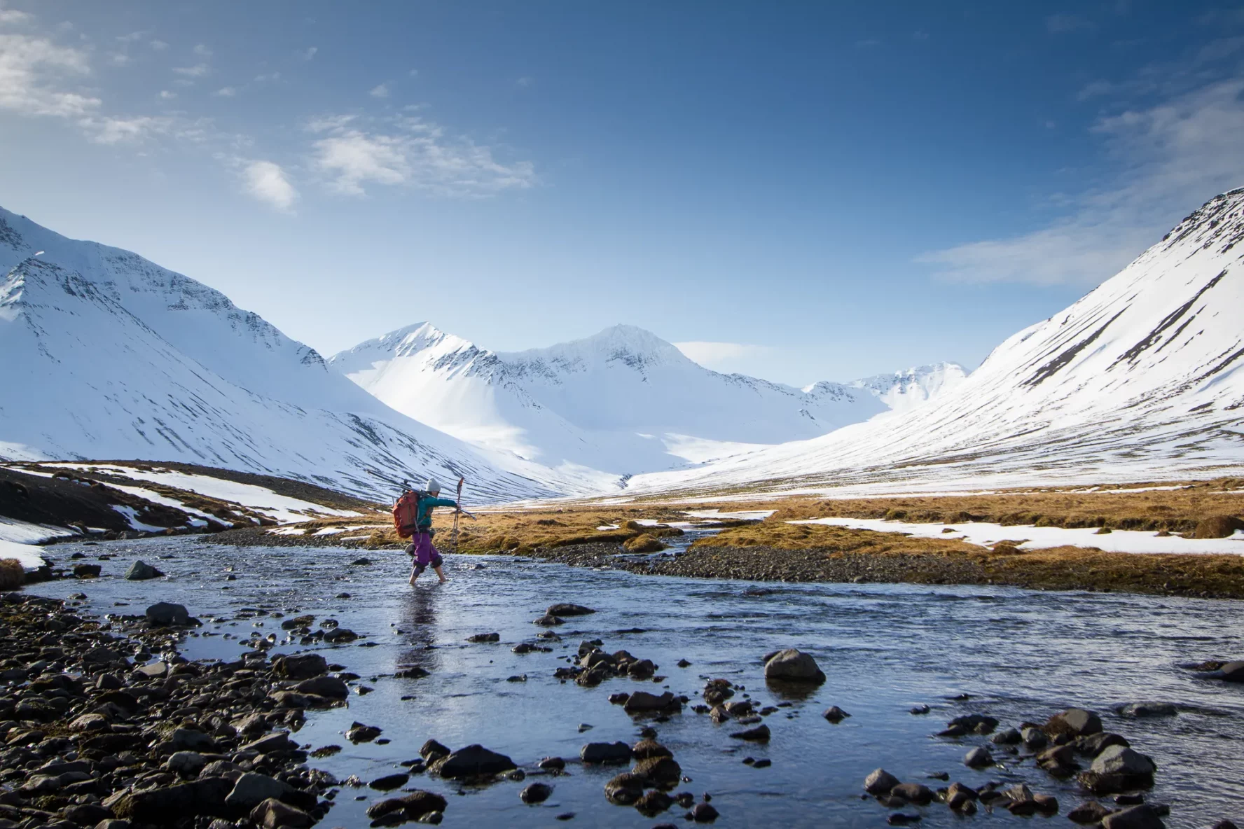 A skier traversing a shallow creek in the Westfjords, Iceland.