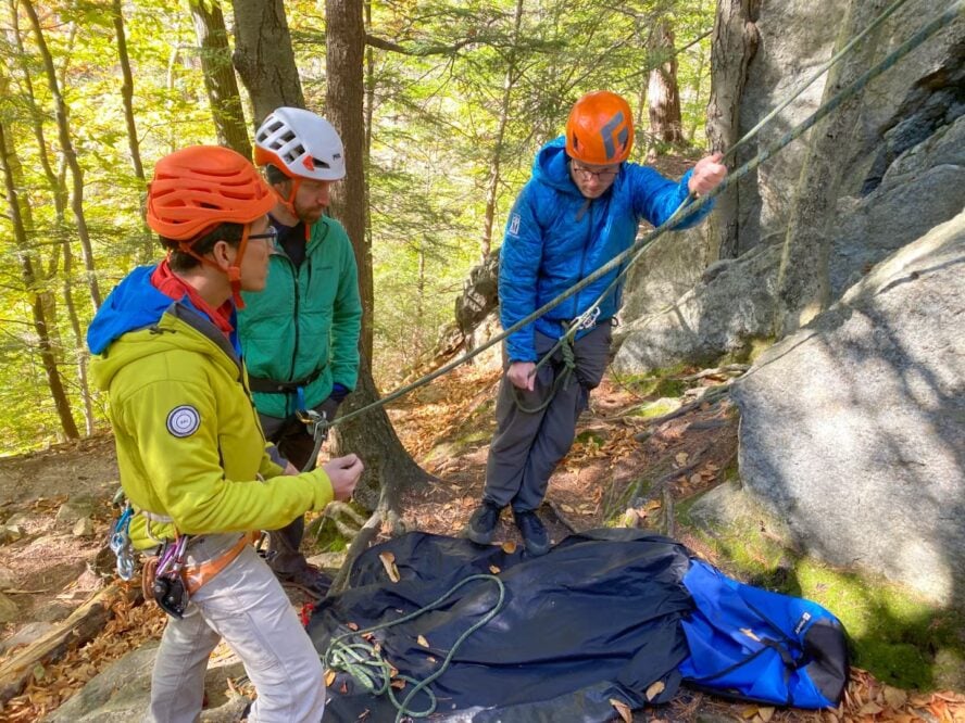 Three climbers taking part in a mountain education and rock climbing program, at the base of a cliff.