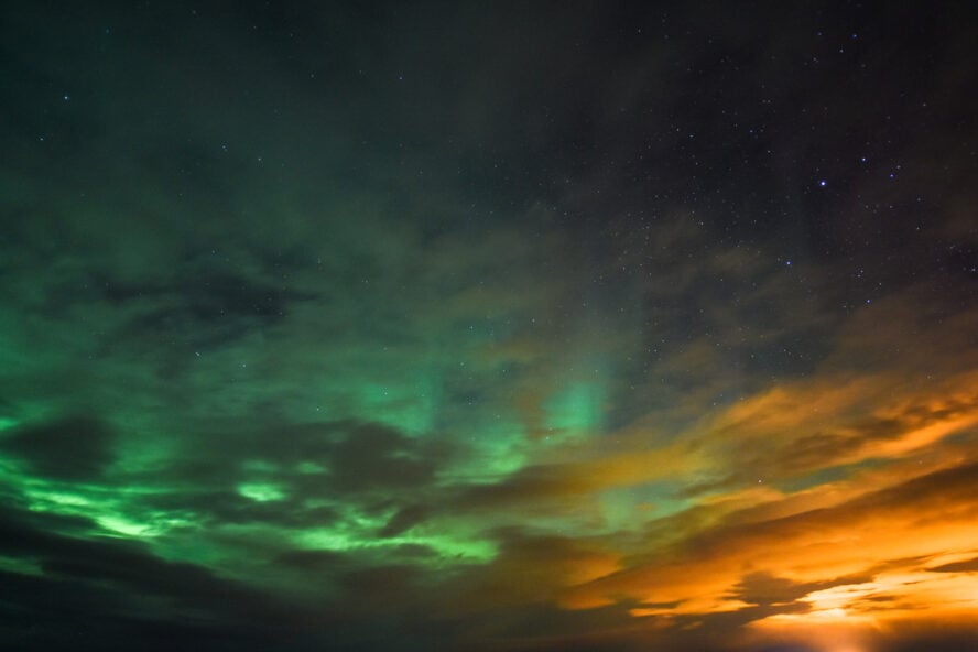 Glowing green and orange northern lights above Reykjavik, Iceland.