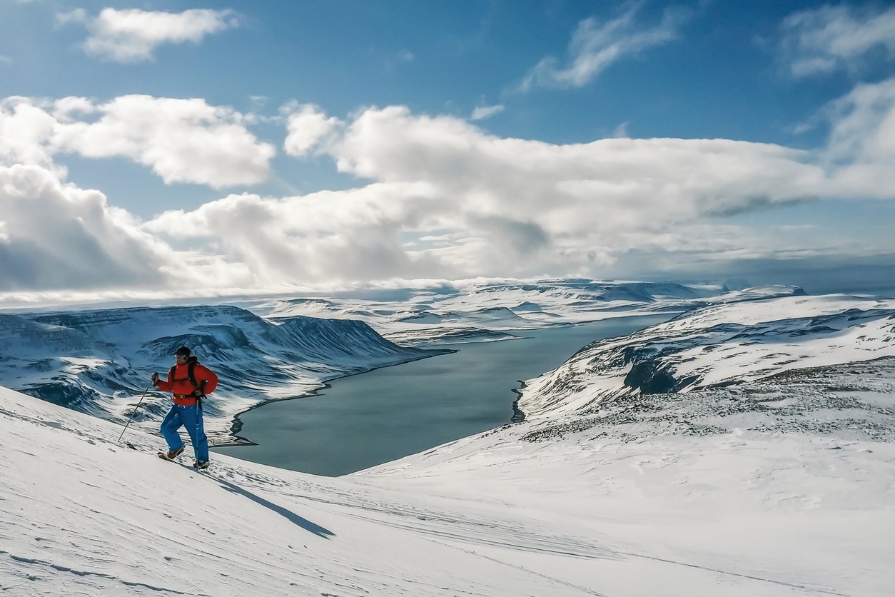 A backcountry skier ascending a mountain in Iceland’s Troll Peninsula, overlooking an impressive fjord.