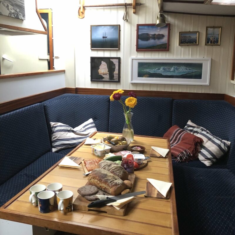 Cozy saloon on Byr sailboat with a wooden dining table and all-around blue booth